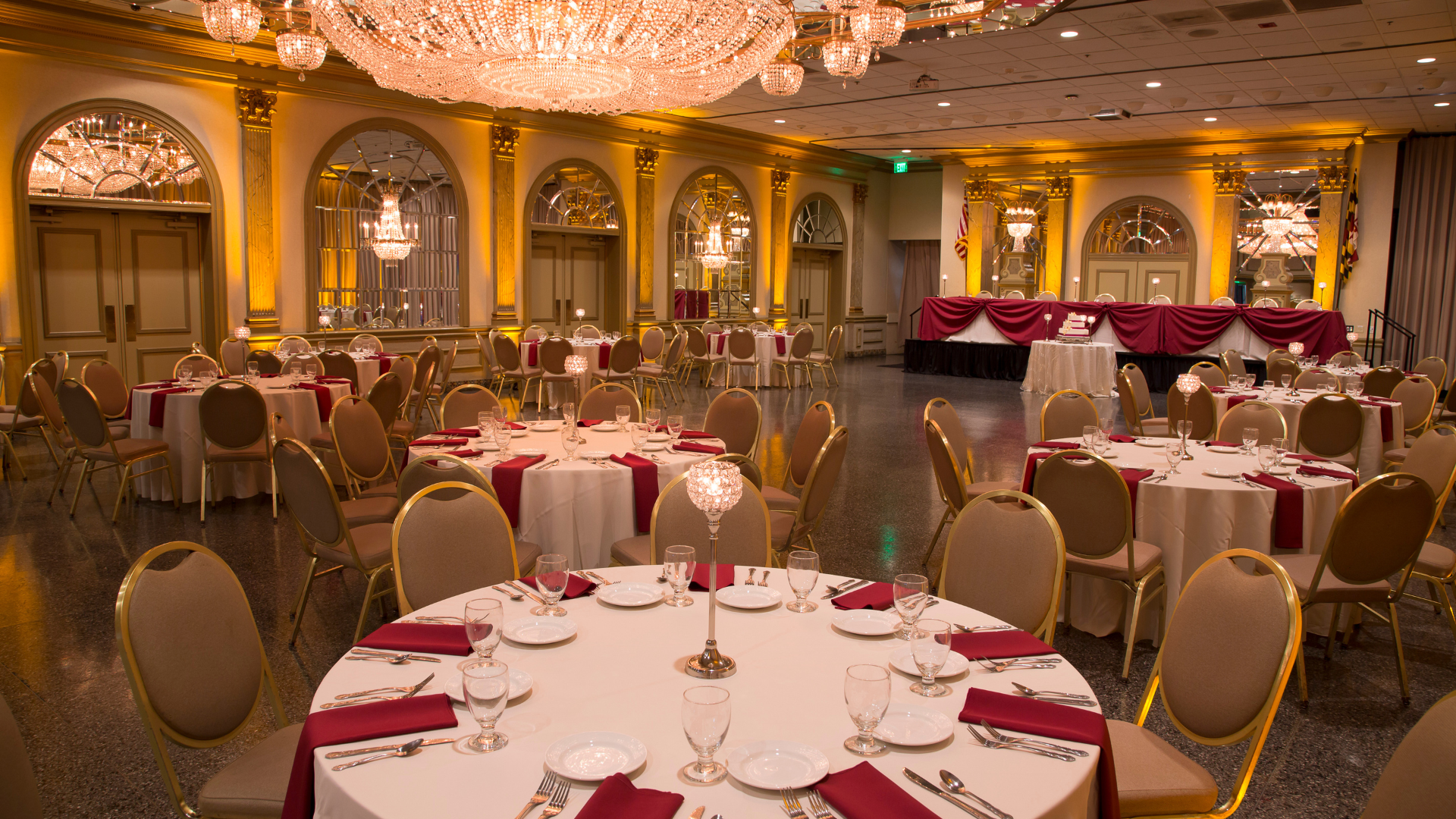 Wedding reception with ivory and burgundy color palette accented with crystal candlesticks and gold uplighting.